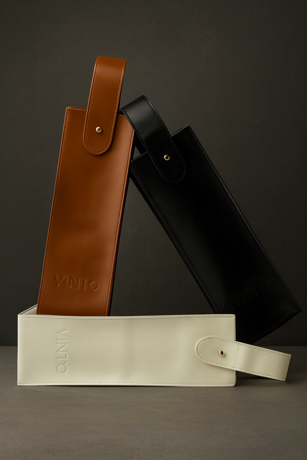 Drei VINTO Weinträgertaschen / Flaschentasche aus hochwertigem Leder  vegan in Braun, Schwarz und Weiß – minimalistisches Design mit edler Prägung und goldenen Knöpfen, vor edlem grauem Hintergrund.